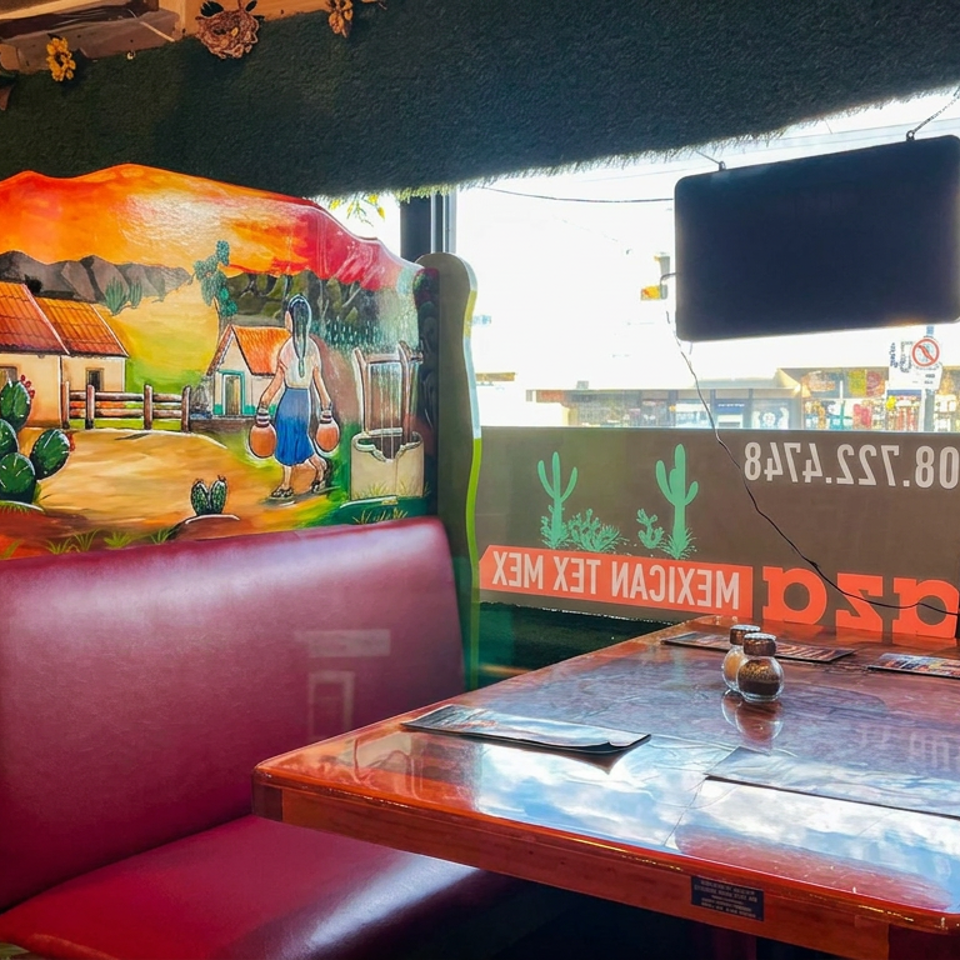 Colorful Mexican restaurant booth with painted rural landscape murals, glossy table, menus, and window signage.